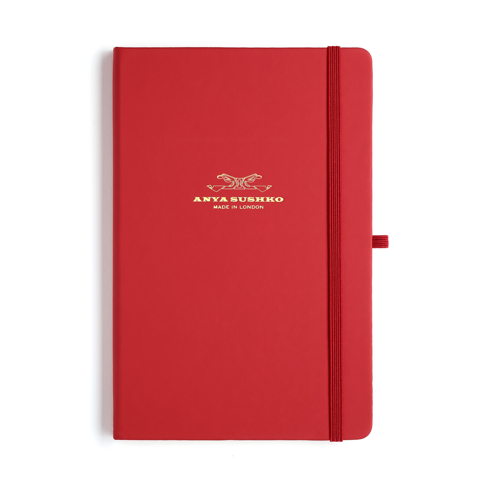 A red hardback A5 refill Luxury notepad with a gold embossed brand logo at the front and a matching elastic pen holder.