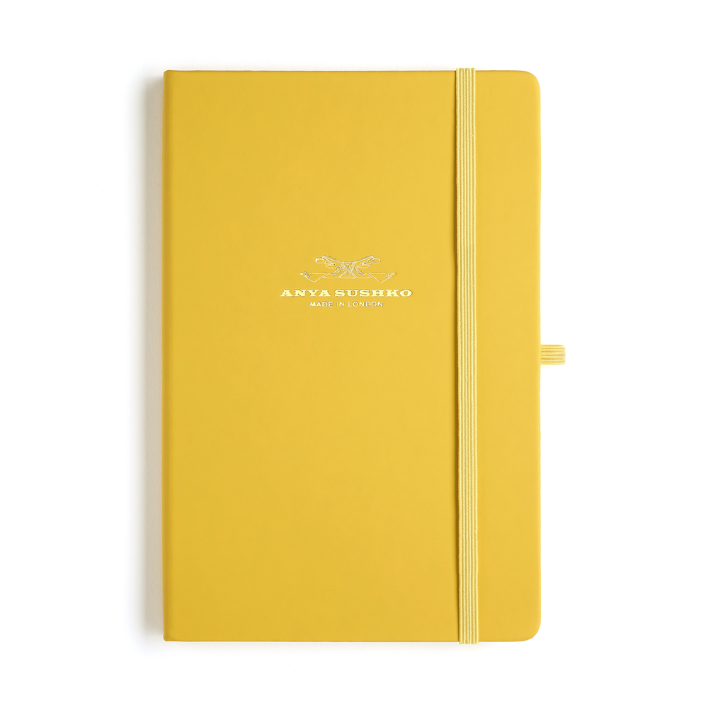 A vibrant yellow hardback A5 refill Luxury notepad with a ribbon bookmark and elastic pen holder, featuring the Anya Sushko brand logo embossed in gold at the front.